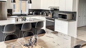 A modern kitchen with a central island, black pendant lights, and white cabinetry. - The Double Diamant (St-Côme)