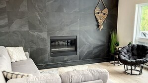 A modern living room with a gray sectional sofa, a black leather chair, a stone wall, and a fireplace. - The Double Diamant (St-Côme)