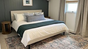 Ein Schlafzimmer mit einem Bett, zwei Nachttischen, einem Deckenventilator, einem Fenster mit Vorhängen und einem gerahmten Bild an der Wand.