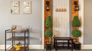A hallway with a brick wall, a white door, two wall-mounted signs, a metal shelf with decorative items, and two potted plants. - Lovely 2 bedroom downtown Three Rivers, sleeps 6 (Three Rivers)