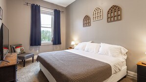 A bedroom with a bed, a desk, a chair, a window with curtains, and decorative wall elements. - Lovely 2 bedroom downtown Three Rivers, sleeps 6 (Three Rivers)
