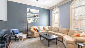 A living room with a sectional sofa, a coffee table, a TV stand, and a ceiling fan. - Lovely 2 bedroom downtown Three Rivers, sleeps 6 (Three Rivers)