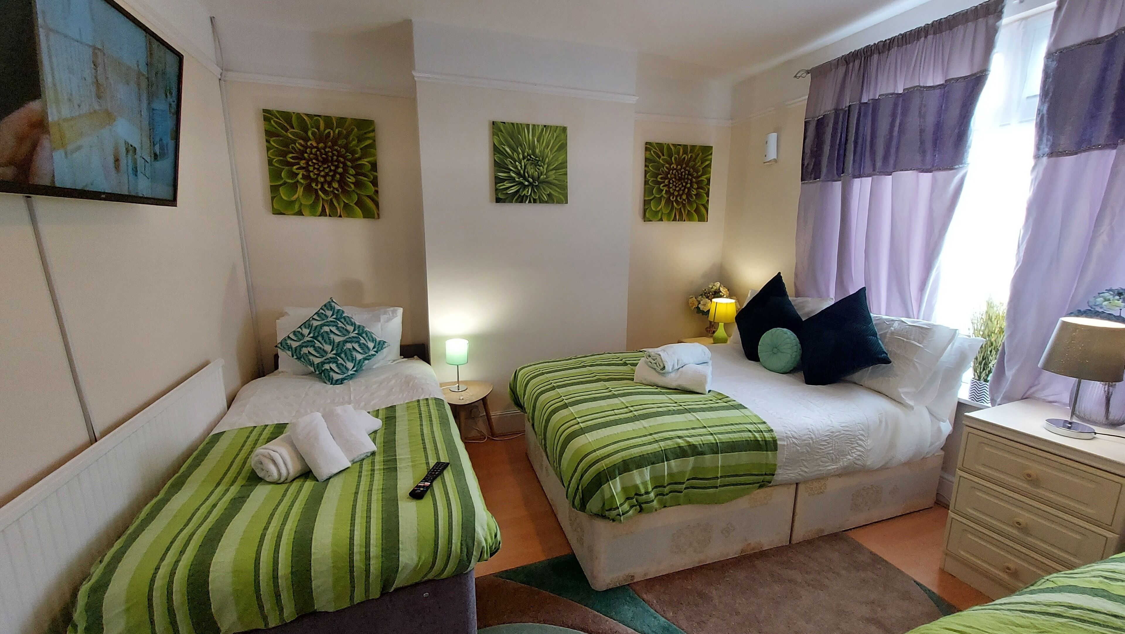 A hotel room with two single beds, a nightstand with a lamp, a dresser, and artwork on the walls.