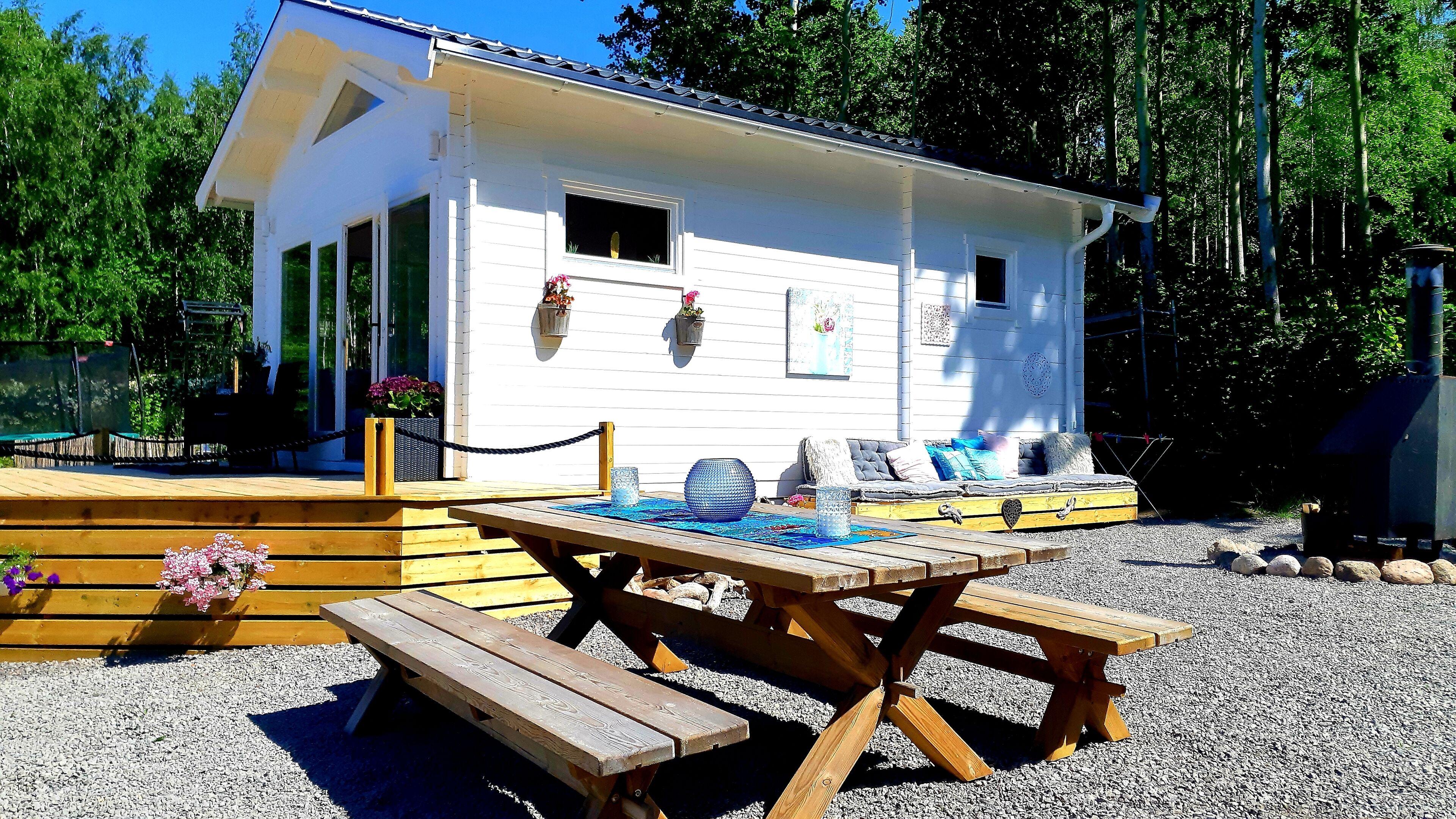 A white cabin with a porch, a wooden table, and benches.
