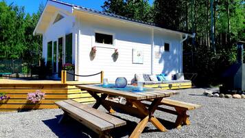 A white cabin with a porch, a wooden table, and benches.