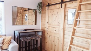 A room with a wooden door, a mirror, a small table with a fur throw, and a view through a window. - Tree of Life Lakeview Loft Retreat (Finnerödja)