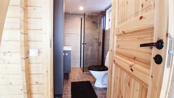 A wooden door leading to a bathroom with a toilet, a shower, and a tiled floor.