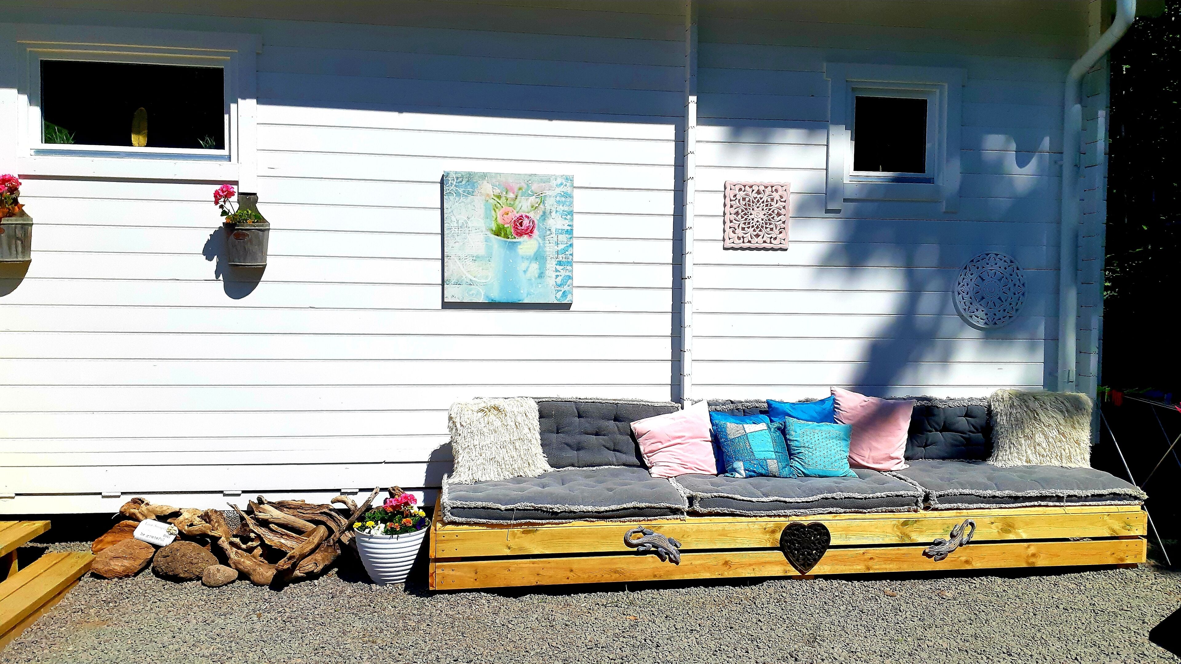 A rustic outdoor seating area with a wooden bench and cushions, surrounded by decorative elements like a potted plant and a wooden log.