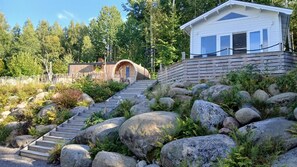 A cabin with a wooden staircase leading to a door, surrounded by large rocks and greenery. - Lakeview Loft, Private Retreat at Lake Skagern (Finnerödja)