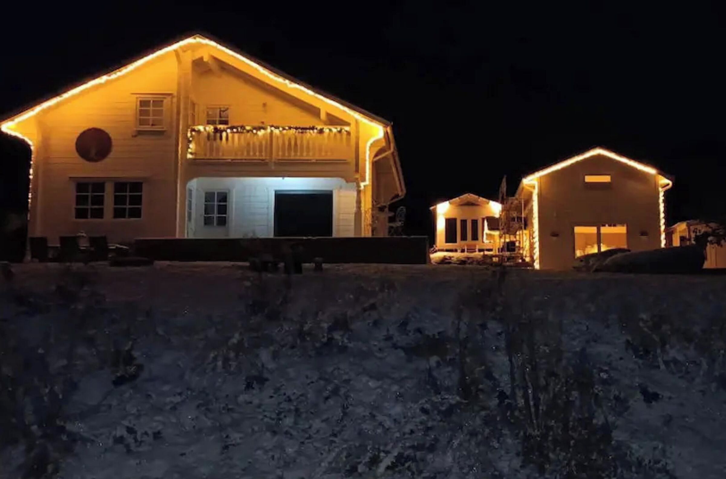 A large, two-story building with a balcony and a garage, illuminated by warm lights.