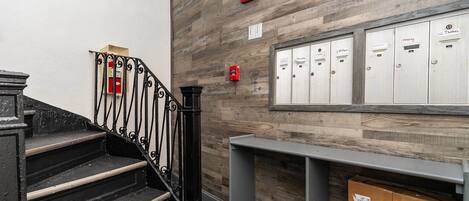 A staircase with black iron railings, a wooden wall with lockers, and a fire alarm on the wall.