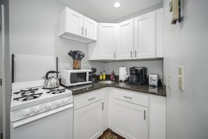 A compact kitchen with white cabinets, a gas stove, a microwave, and a toaster. - Exquisite North End 1brm (Boston)