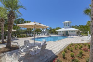 Un espace piscine équipé de chaises longues, de parasols et d’un petit bâtiment surmonté d’une tour.