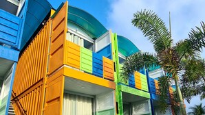 Un edificio colorido con una escalera que lleva a una puerta, rodeado de un césped cuidado y un cielo azul brillante.