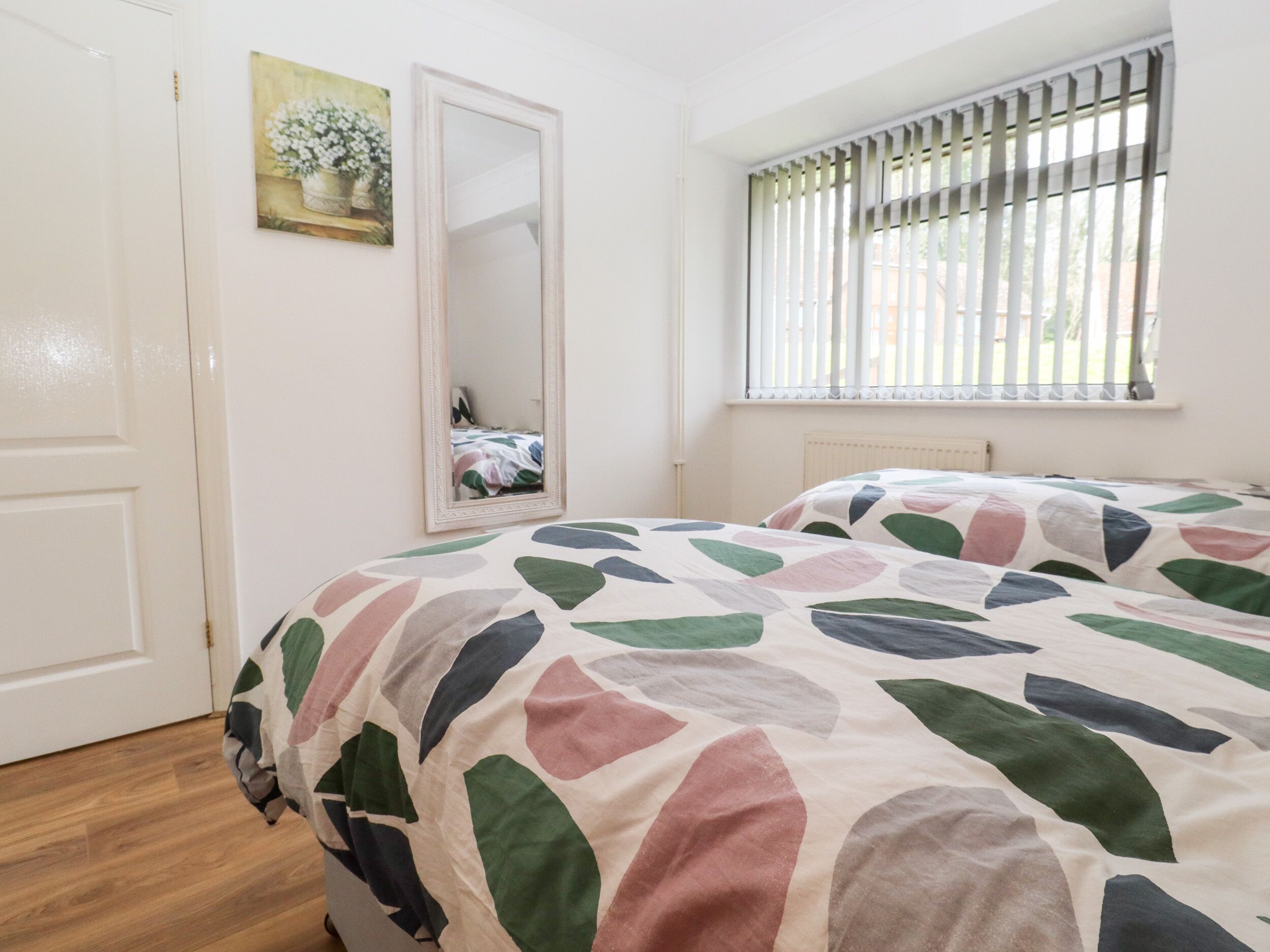 Un dormitorio con una cama, un espejo, una ventana con persianas y un cuadro en la pared.