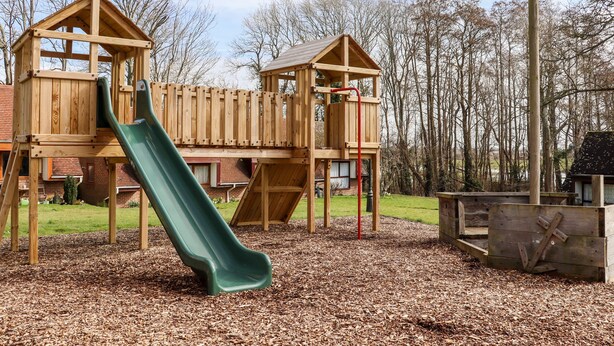 Un parque infantil de madera con un tobogán verde y estructuras para escalar.