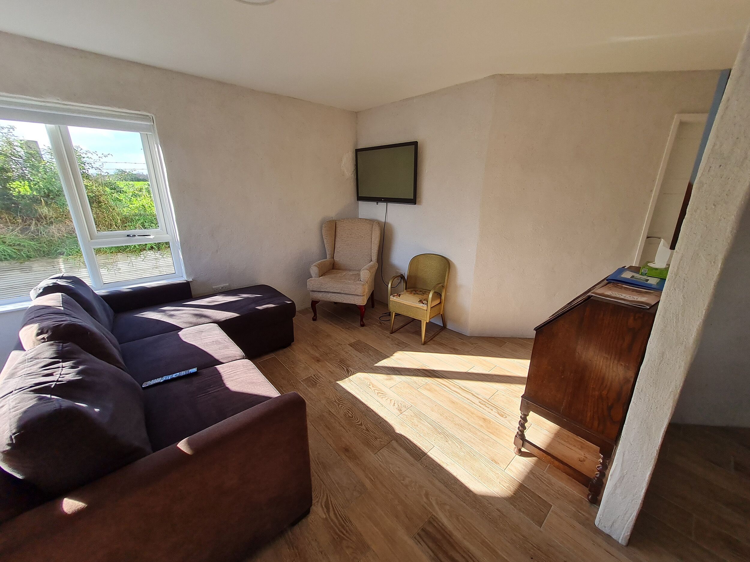 Una sala de estar con un sofá seccional, un sillón pequeño, un aparador de madera y un televisor en la pared.