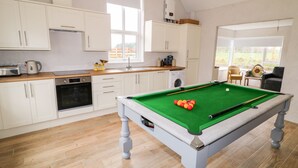 Eine moderne Küche mit Poolbillard, Holzboden und weißen Schränken.