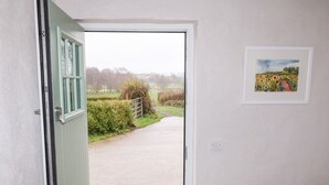 Ein Durchgang zu einer Landstraße mit einer Hecke und einem Tor, ein gerahmtes Bild an der Wand und ein Lichtschalter.