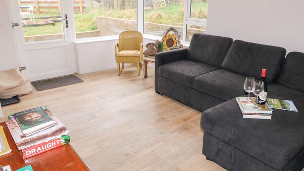 Ein Wohnzimmer mit einer Couch, einem Sessel, einem Couchtisch mit Büchern und Blick durch große Fenster.