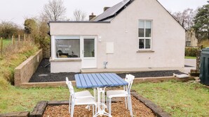 Ein modernes Haus mit Satteldach, einem großen Fenster und einer Terrasse mit Tisch und Stühlen.