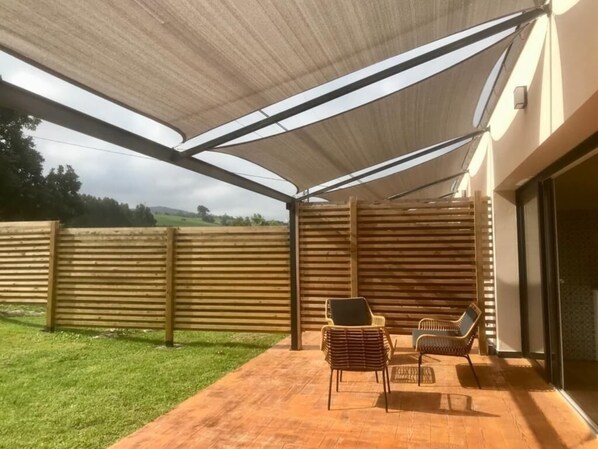 Eine überdachte Terrasse mit zwei Korbstühlen und einer Glastür, die zu einem Zimmer führt.