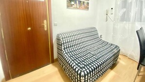 Ein Zimmer mit einer gepolsterten Couch mit Muster, einer Holztür, einer Wandcollage aus Fotos und einem Sessel.