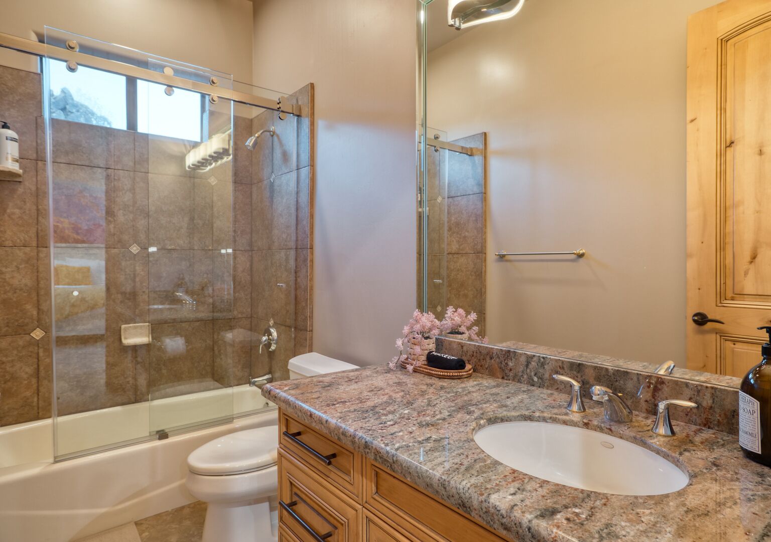 A bathroom with a glass-enclosed shower, a bathtub, a sink with a large mirror, and wooden cabinets.