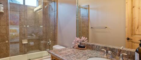 A bathroom with a glass-enclosed shower, a bathtub, a sink with a large mirror, and wooden cabinets.