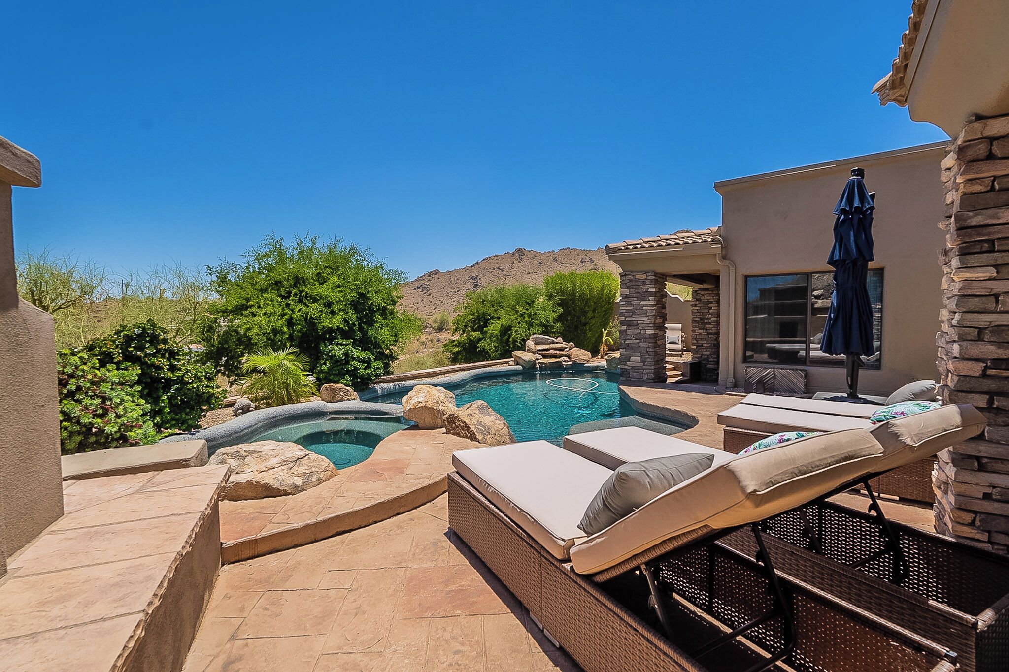A backyard with a swimming pool, lounge chairs, and a stone building.