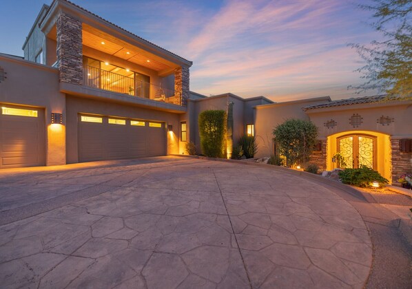 A modern two-story house with a stone facade, a large garage, and a well-lit driveway.