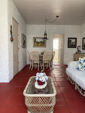 A room with a dining table and chairs, a bed, and a wicker basket with flowers.
