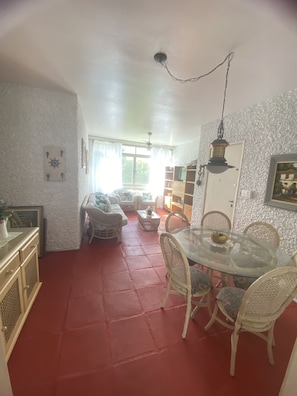 A dining area with a glass table and wicker chairs, a red floor, and a ceiling fan.