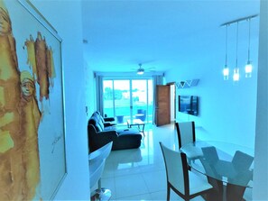 A modern living room with a sofa, dining table, chairs, and a TV mounted on the wall. - Near the Beach new and Modern Penthouse Coral H3 (Puerto Plata)