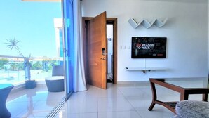 A modern living room with a large TV, a balcony with potted plants, and a view of the city. - Near the Beach new and Modern Penthouse Coral H3 (Puerto Plata)