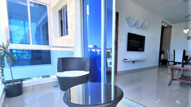 A modern indoor space with a glass table and wicker chairs, a potted plant, and a view through large windows. - Near the Beach new and Modern Penthouse Coral H3 (Puerto Plata)