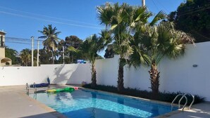 A swimming pool with palm trees, a white wall, and a clear blue sky. - Near the Beach new and Modern Penthouse Coral H3 (Puerto Plata)