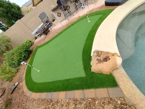 A swimming pool with a curved edge, surrounded by a landscaped area with artificial grass and a rock feature.