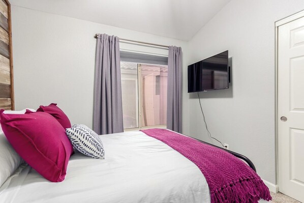 A bedroom with a bed, a TV mounted on the wall, and a window with curtains.