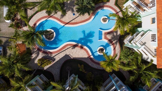 An aerial view of a resort with a central swimming pool, surrounded by palm trees and a tiled walkway. - Huge Penthouse Near the Beach With Private Jacuzzi (Punta Cana)