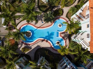 An aerial view of a resort with a central swimming pool, surrounded by palm trees and a tiled walkway. - Huge Penthouse Near the Beach With Private Jacuzzi (Punta Cana)