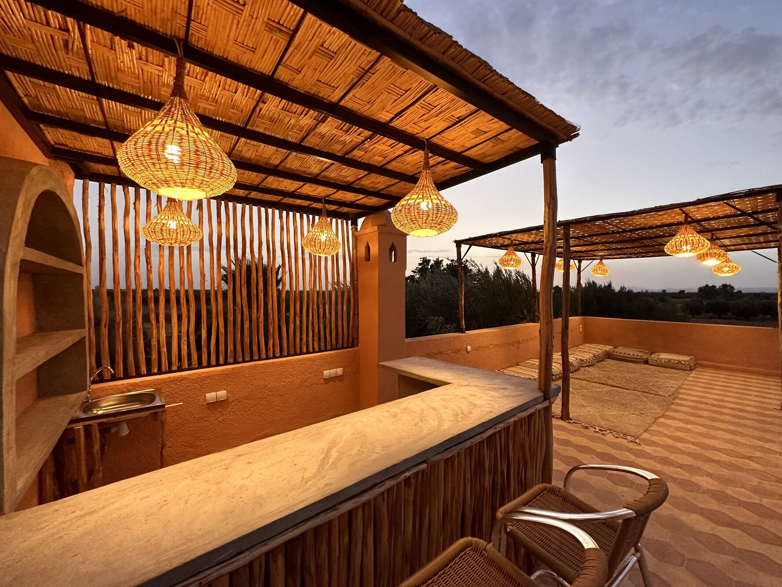 Une terrasse extérieure dotée d’une pergola en bois, de chaises en osier et de guirlandes lumineuses.
