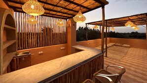 Eine Terrass mit Holzpergola, Korbstühlen und hängenden Lichterketten.
