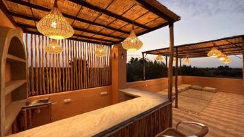 Une terrasse extérieure dotée d’une pergola en bois, de chaises en osier et de guirlandes lumineuses.