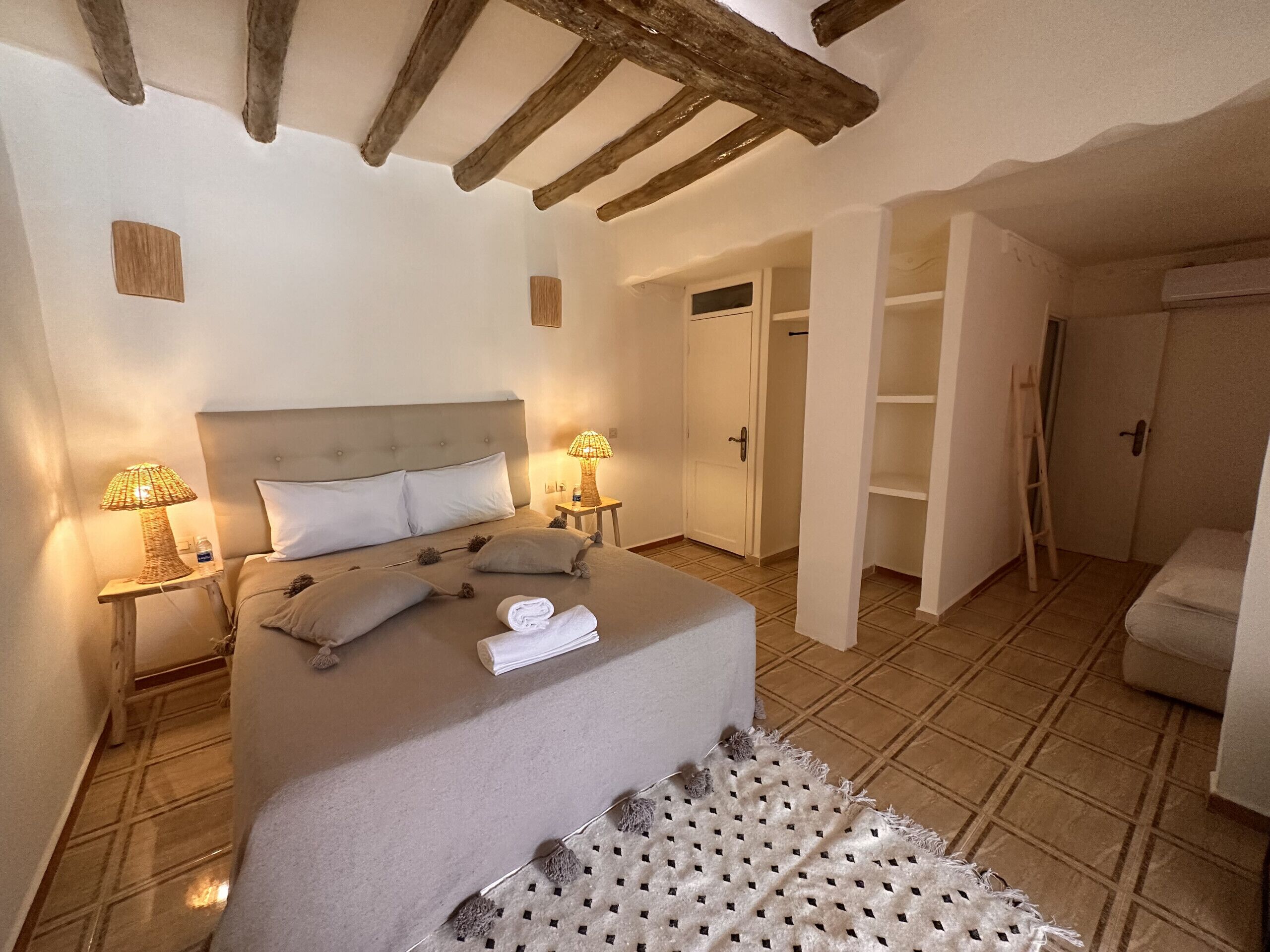Une chambre à coucher avec un grand lit, deux tables de chevet avec des lampes, une armoire et une porte donnant sur une autre pièce.