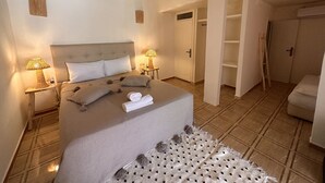 Ein Schlafzimmer mit einem großen Bett, zwei Nachttischen mit Lampen, einem Kleiderschrank und einer Tür zu einem anderen Raum.