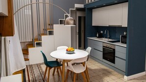 A modern kitchen with white cabinets, a built-in oven, and a dining area with a round table and chairs. - Opera Suites - Tosca (Palermo)