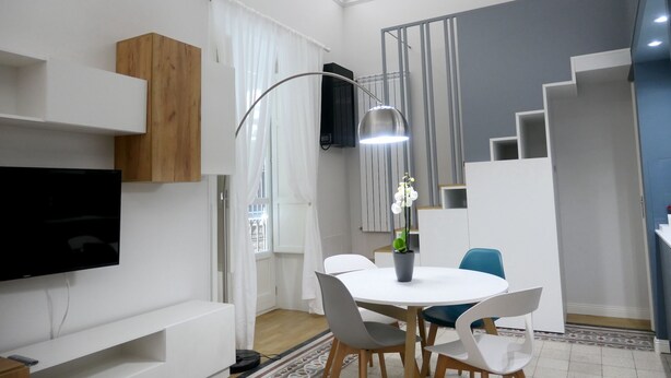 A modern living room with a flat-screen TV, a dining table with chairs, a staircase, and a ceiling with intricate design. - Opera Suites - Tosca (Palermo)