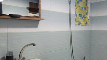 A bathroom with a white sink, a mirror, and a shower with a hose.