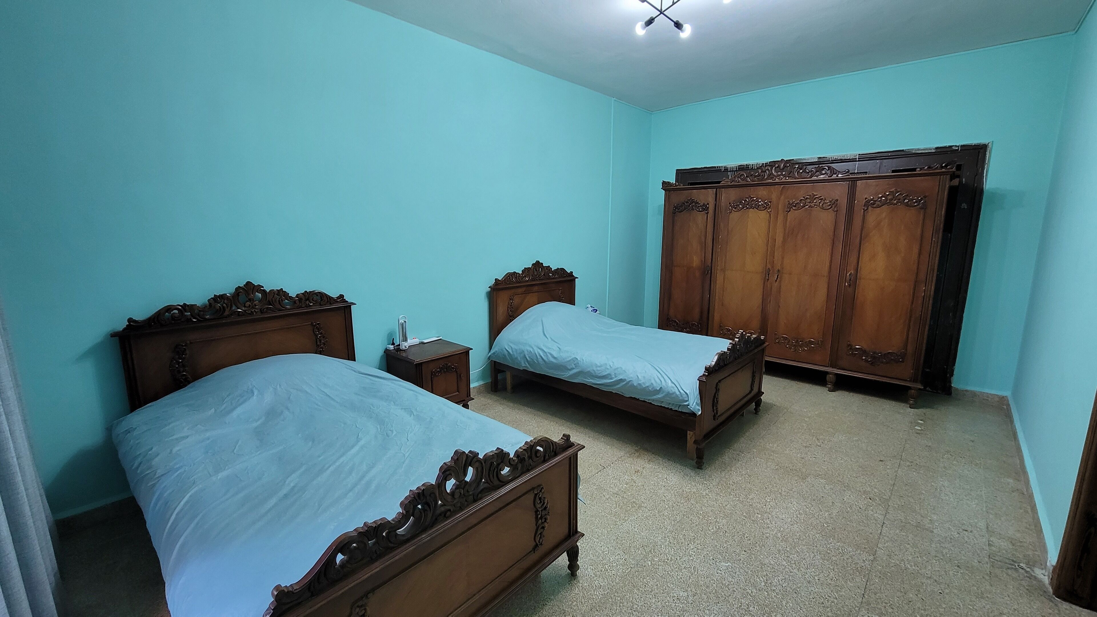 A bedroom with two wooden beds, a wardrobe, and a bedside table.